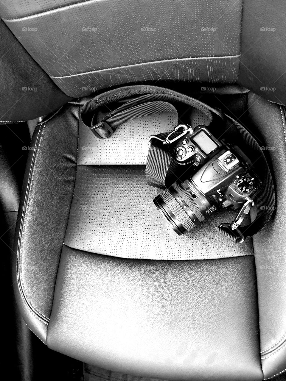 A professional camera sits in a classical flat lay in a black and white car seat.