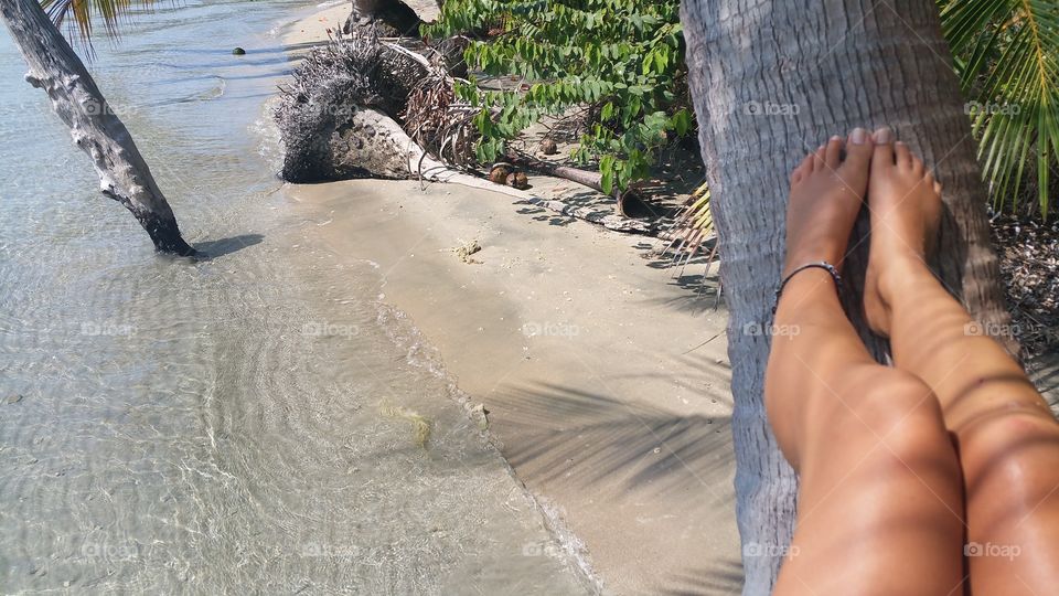 Girls tanned legs on a tree on a deserted tropical paradise beach.