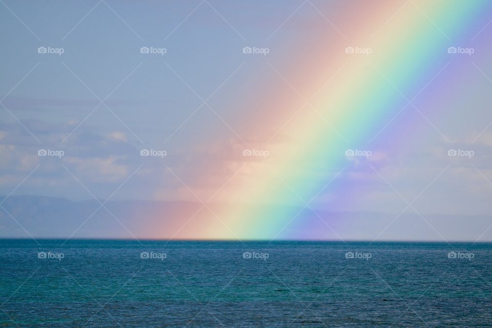 Large rainbow closeup over ocean horizon on black stormy day