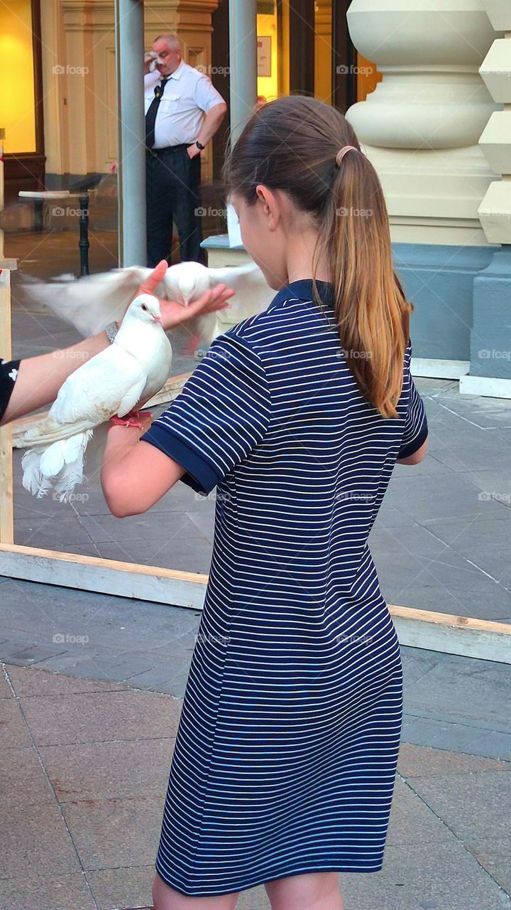 Summer evening.  A girl in a dress with two white doves in her arms.  Hot evening.  In the background, a guard is wiping sweat from his face with a handkerchief.