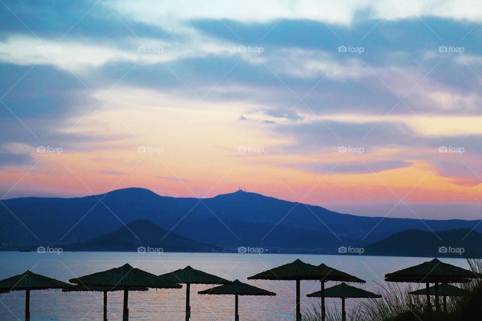 Beautiful sky over the blue mountains behind the parasols at the beach by the blue water