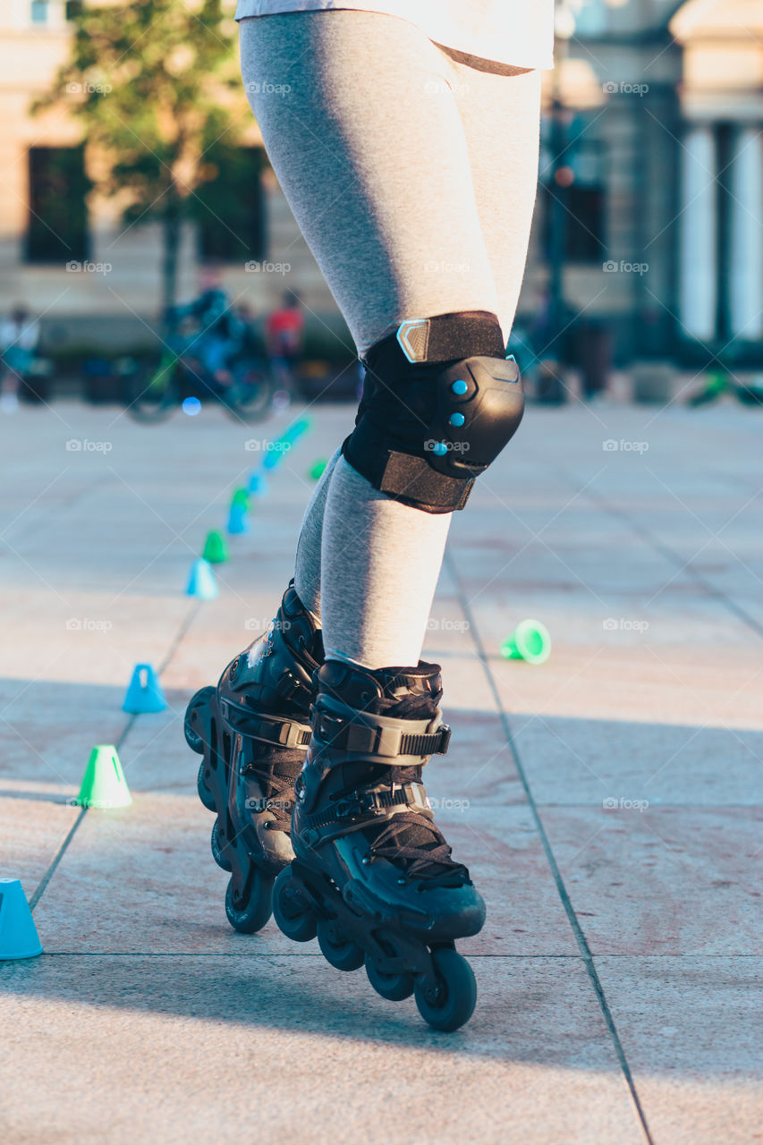 Young girl training the riding on roller skates. Closeup of female legs with roller skates and protectors