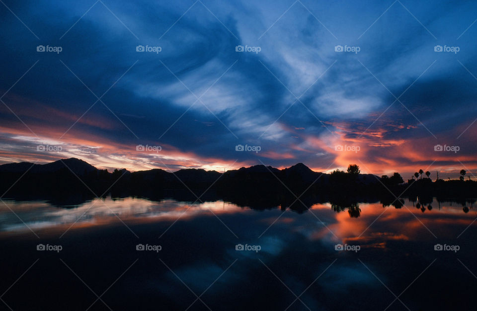 A beautiful western sunset with gradient shades of blue and orange from the suns light casts its reflection onto a pond.