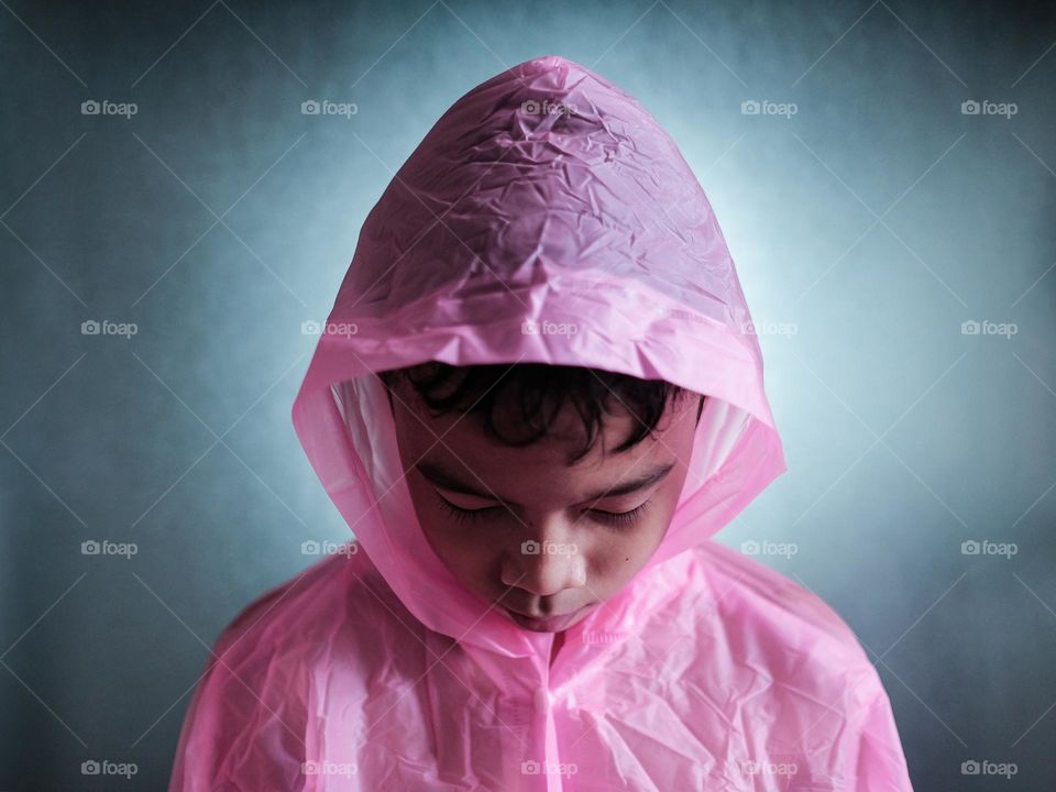 A boy is trying on a pink raincoat against back lighted frosted glass wall