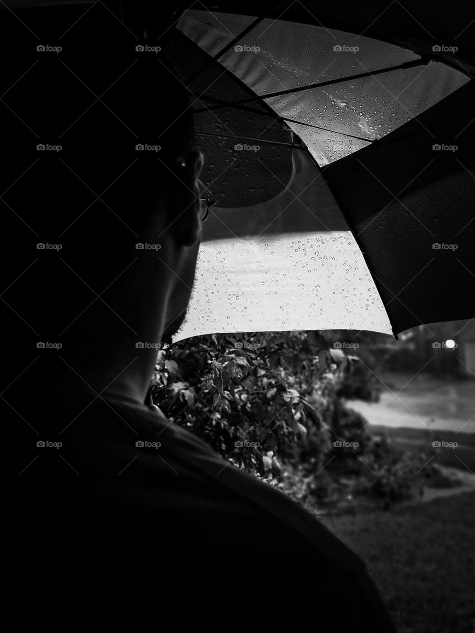 Sadness depicted in black and white with a man looking away on a gloomy rainy day while holding an umbrella.