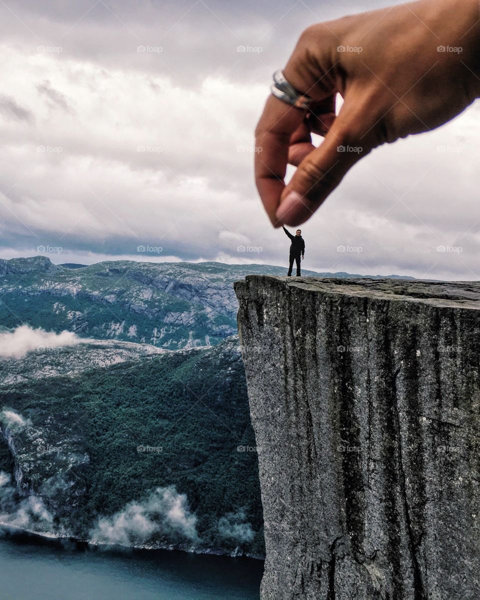 Huge uand from above holding a tiny figure standing on the edge of Prekestolen rock.