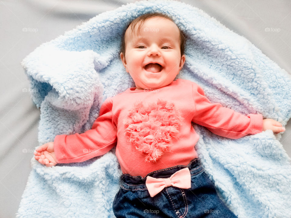 My heart beating. Happy smiling baby girl lying on blanket. She is wearing body suit with heart shape and blue jeans with bow tie