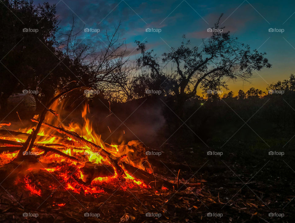 A bonfire at dusk, orange flames contrast with the twilight blue sky