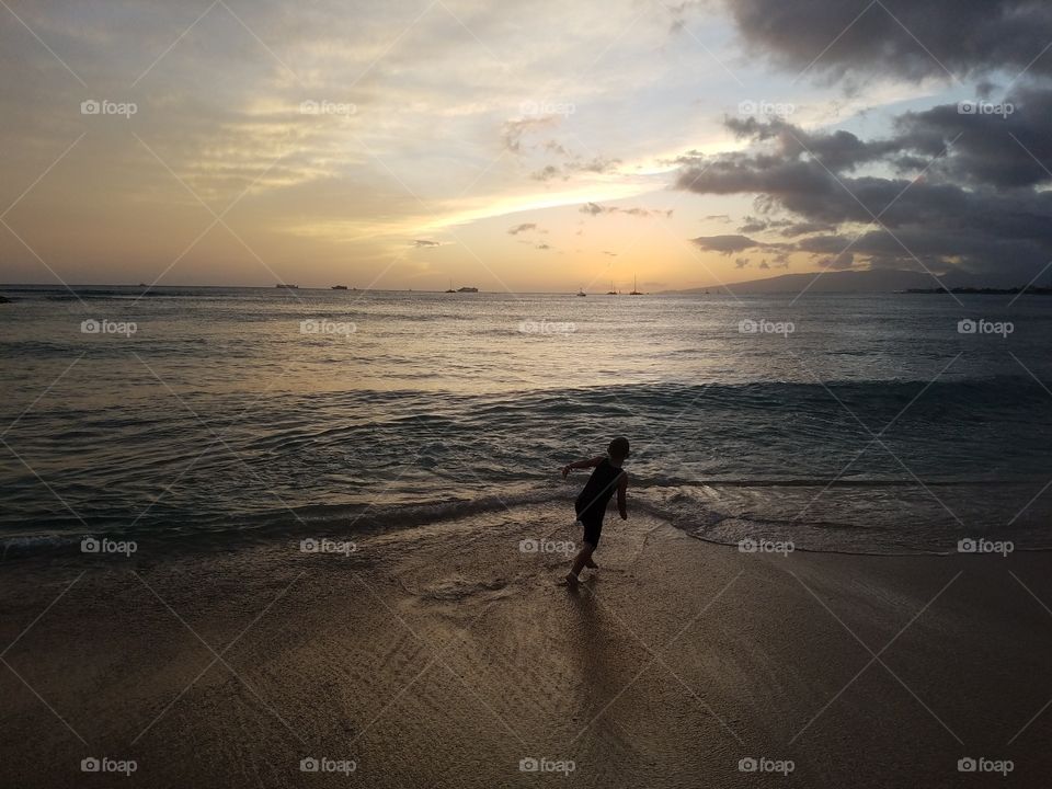 Boy runs from waves as they crash ashore beneath waikiki sunset