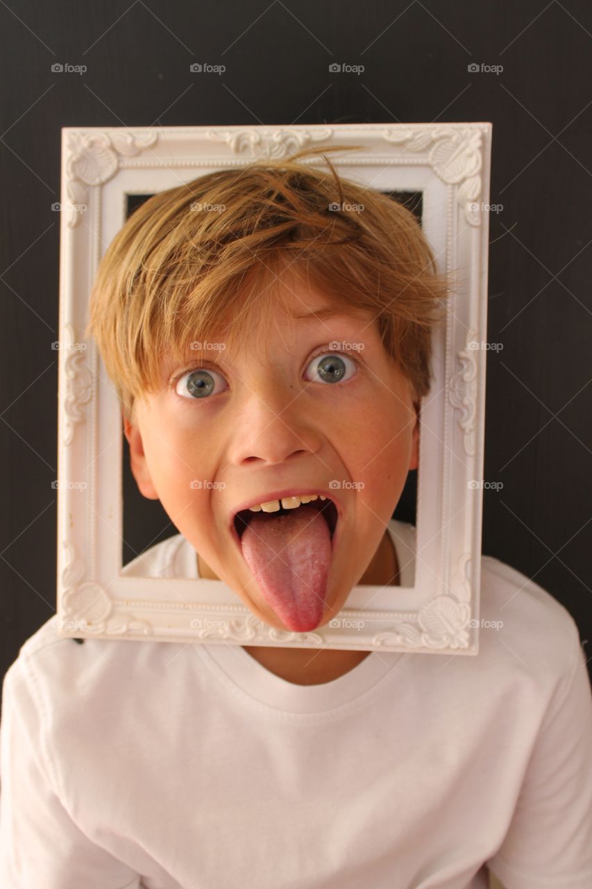 Portrait of a boy sticking out tongue with empty photo frame