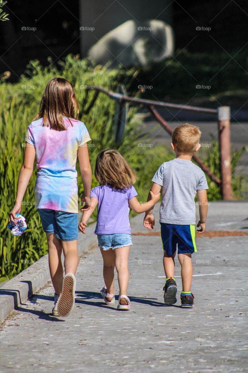Three kids walking along a grassy lake on a warm summer day in Oregon 