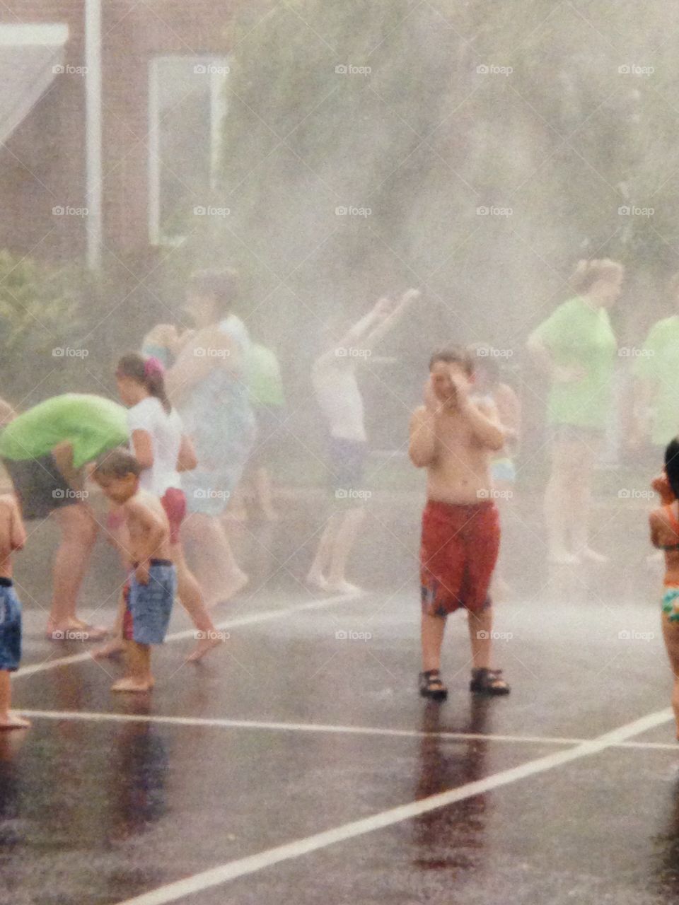 Children standing in rainy mist water from fire truck 