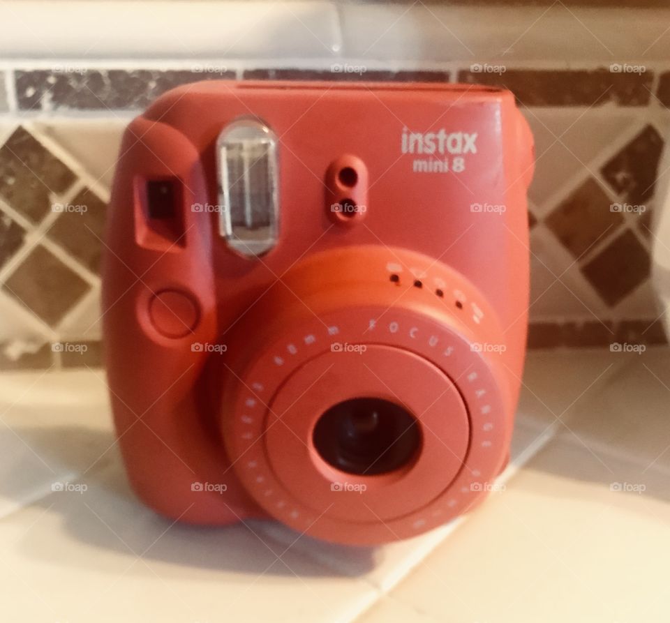 A coral colored,  peach colored I stax mini 8 polaroid camera on display  