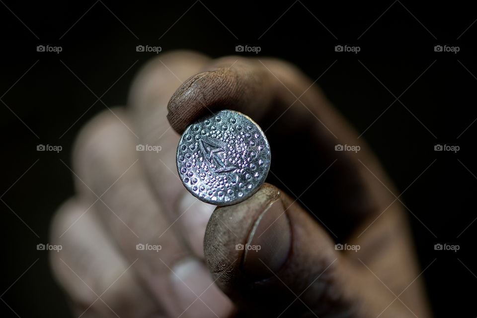 Close-up dirty blacksmith fingers hold a horoscope Sigittarius metal symbol