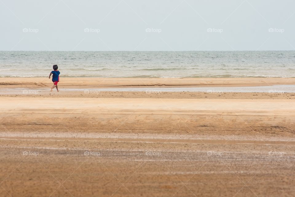 An excited child playfully runs along the beach to towards the sea. 