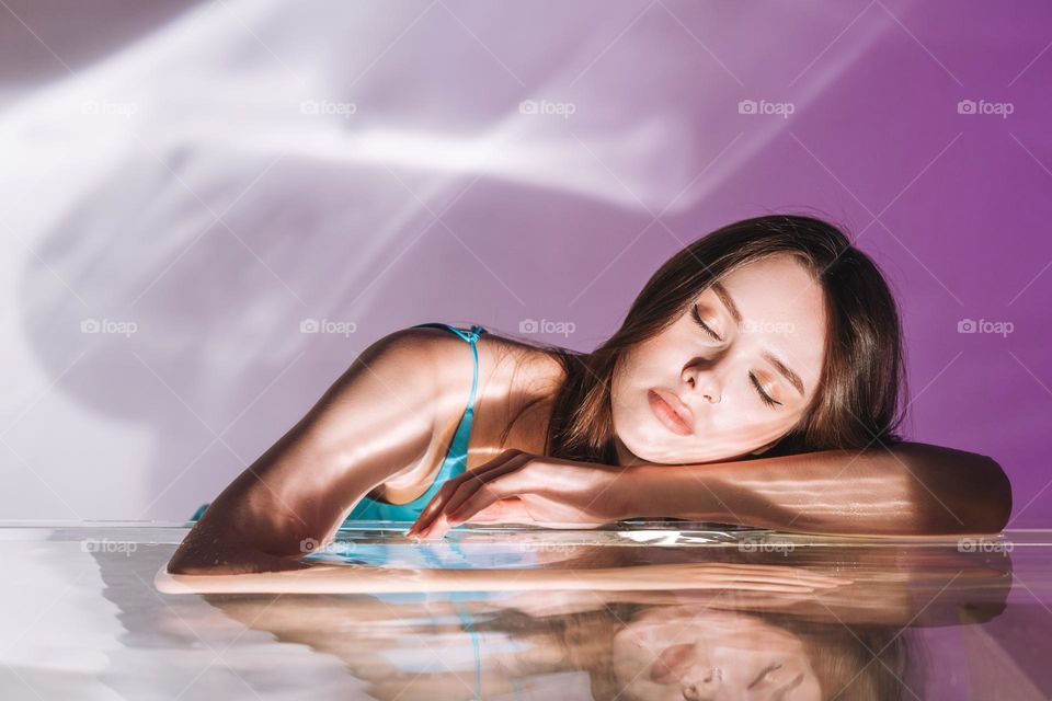 Beauty portrait with water of young woman fashion model with closed eyes with healthy dark long hair on purple background