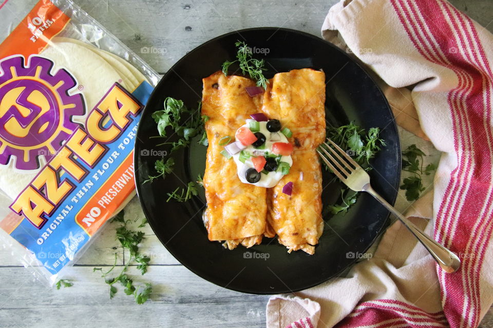 Chicken enchiladas on black plate with vegetables and wooden background 