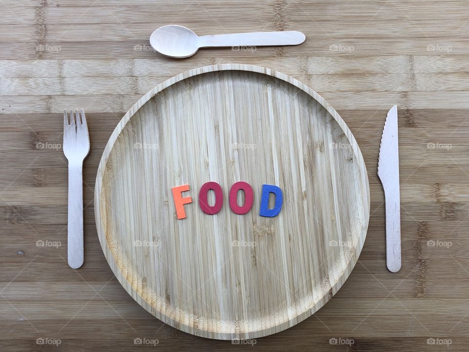 wooden dish with wooden cutlery over a wooden table abd colored wooden letters for the word Food