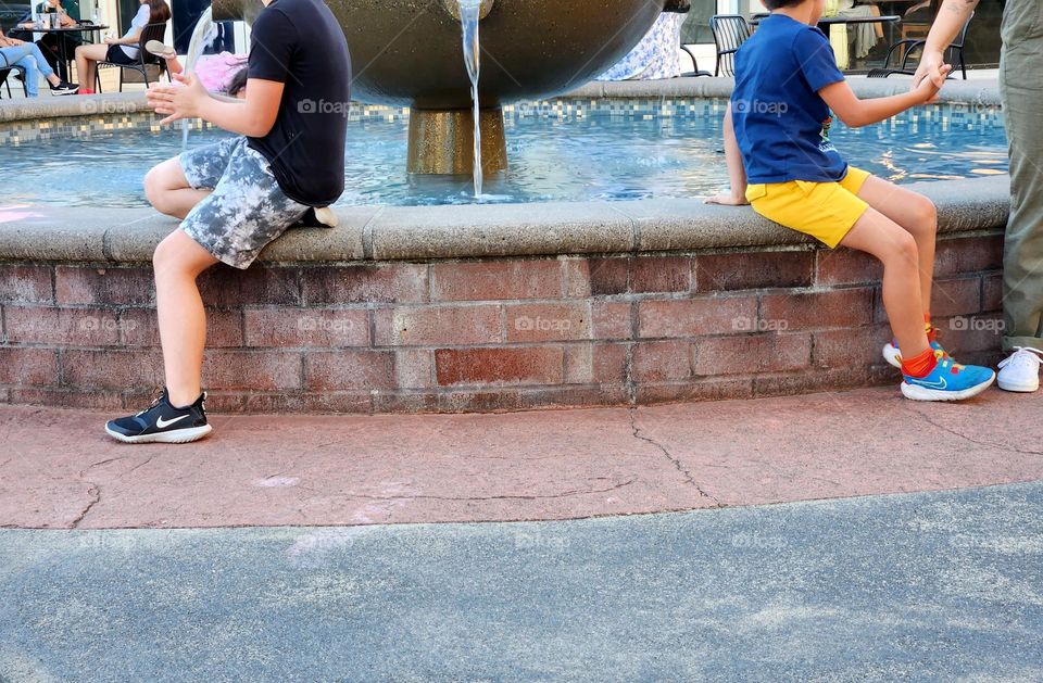 two boys wearing t-shirts and shorts enjoying the cool water of a fountain on a hot Summer evening in Oregon