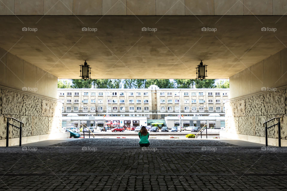 The woman is sitting on the step and watching the apartment block