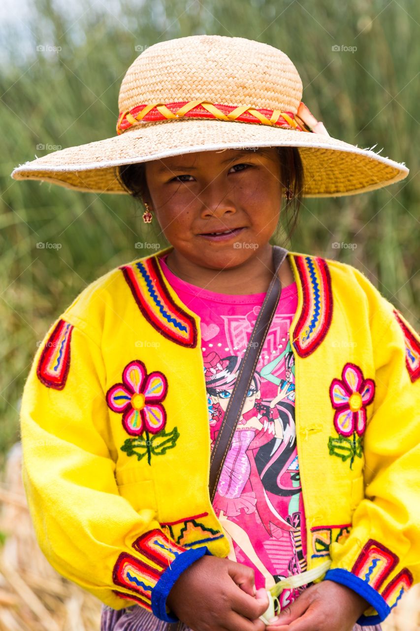 Peruvian girl posing. Young Peruvian girl posing for camera. Traditional hat and colorful shirt. Green straw background out of focus.
