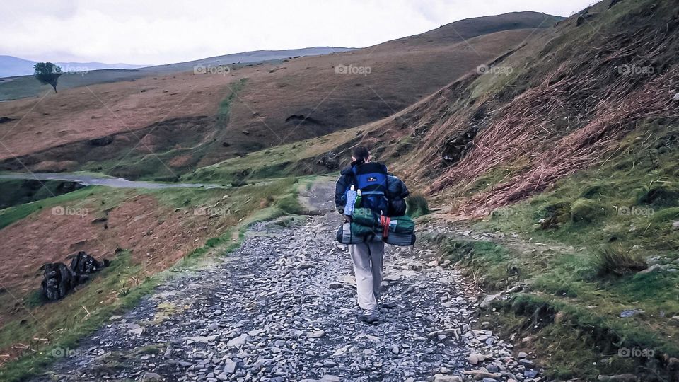 A man with lots of hiking equipment makes his way along a trail in the Lake District of England 