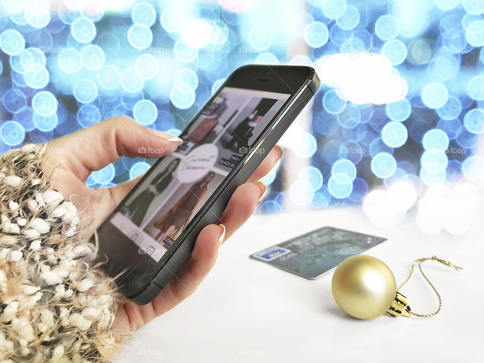 Christmas holiday shopping using mobile phone in front of blue bokeh lights background 