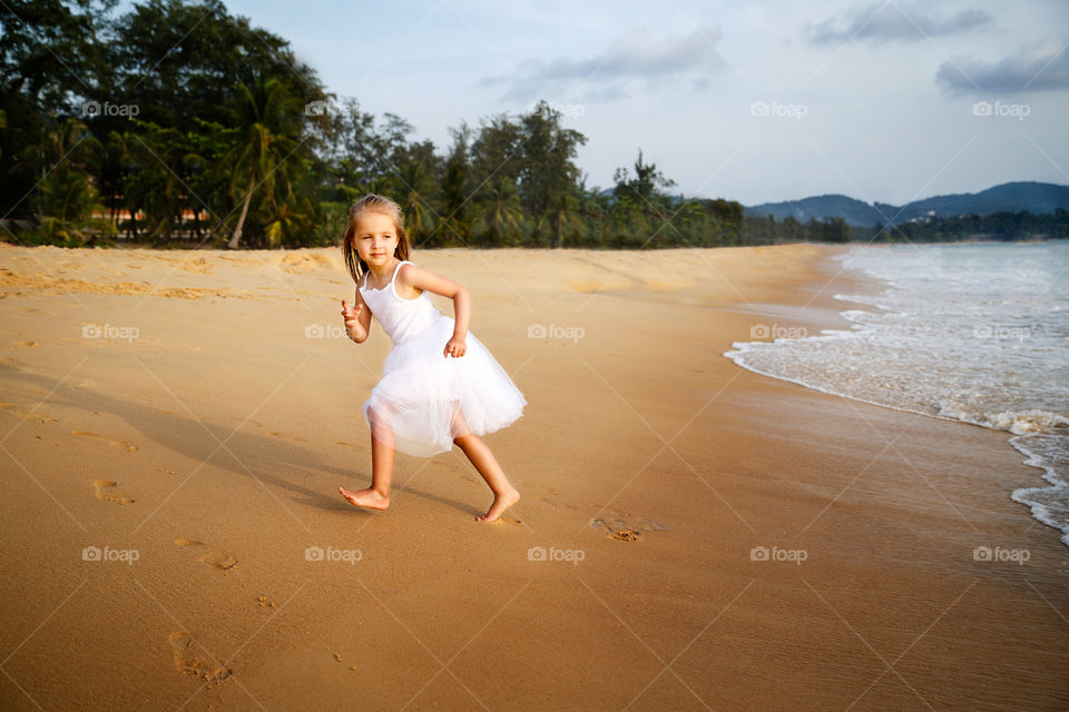 Cute little girl with blonde hair running on the sandy beach 