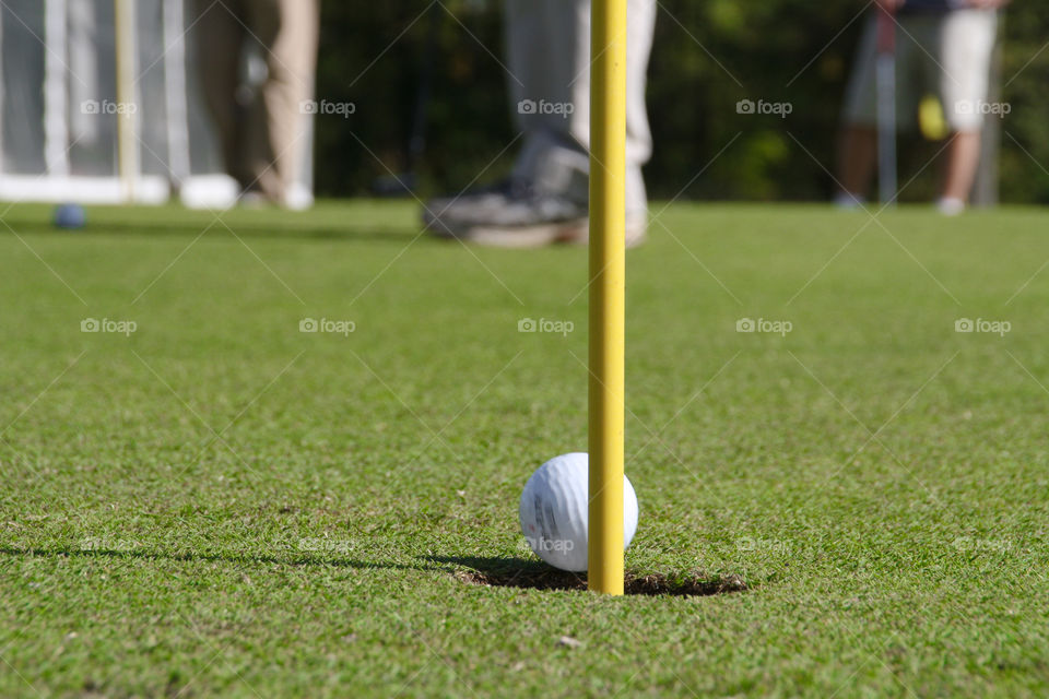 A gold ball rolls into the hole across the green with a golfer in the background