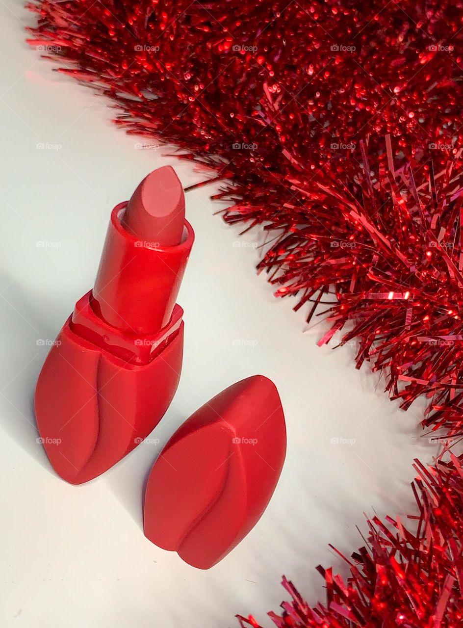 Red lipstick in a lip shaped container with a red tinsel background 
