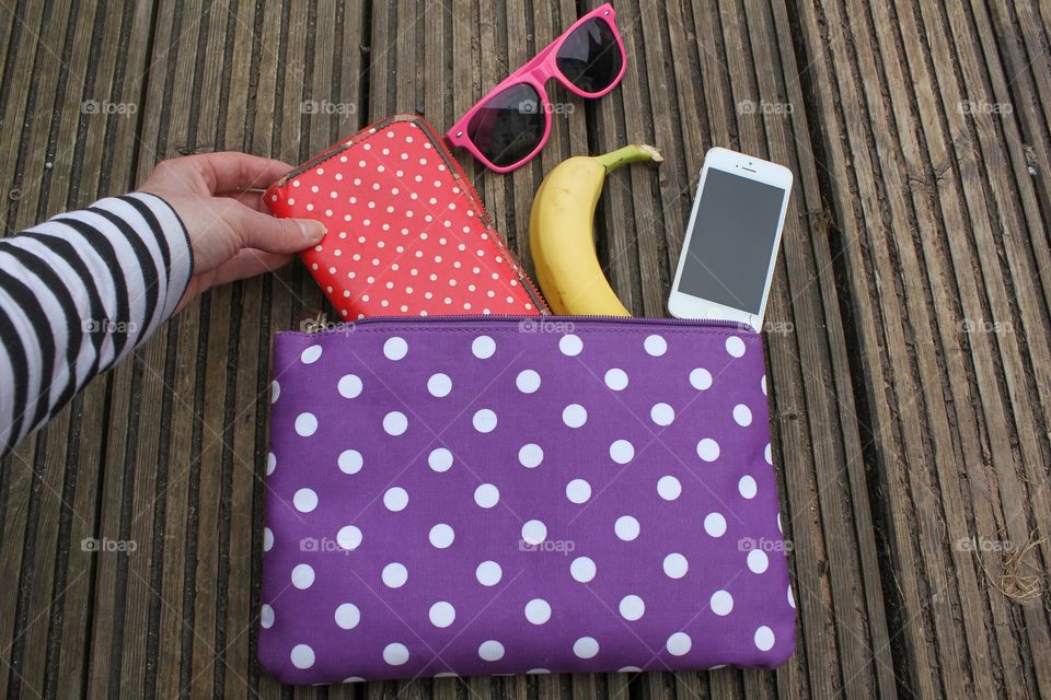 Hand grasping a purse from a spotty bag with a healthy snack and sunglasses 