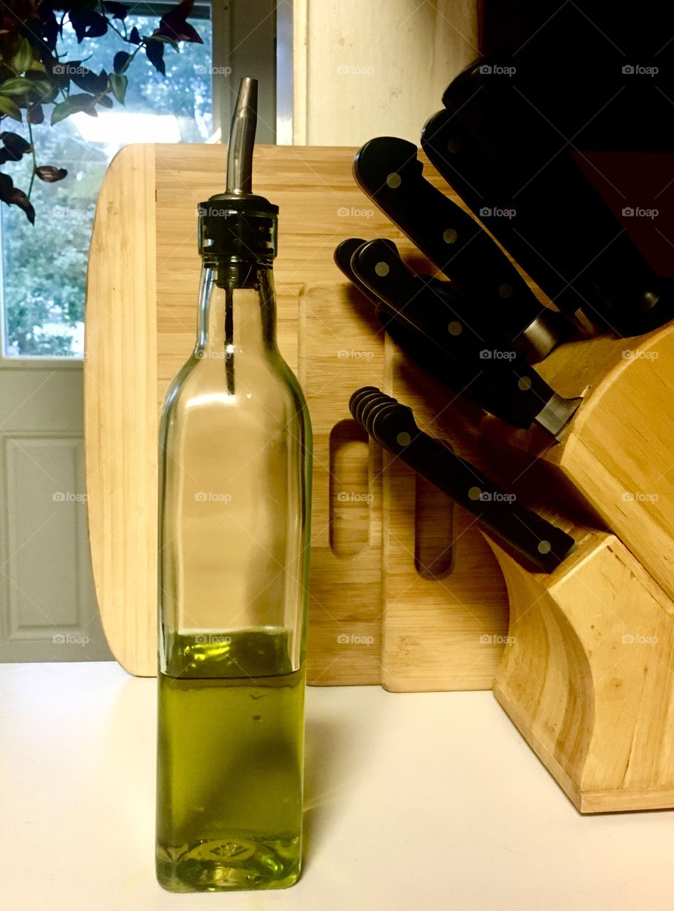 High quality olive oil in a glass container with wood cutting boards and cutlery in the background in a kitchen 