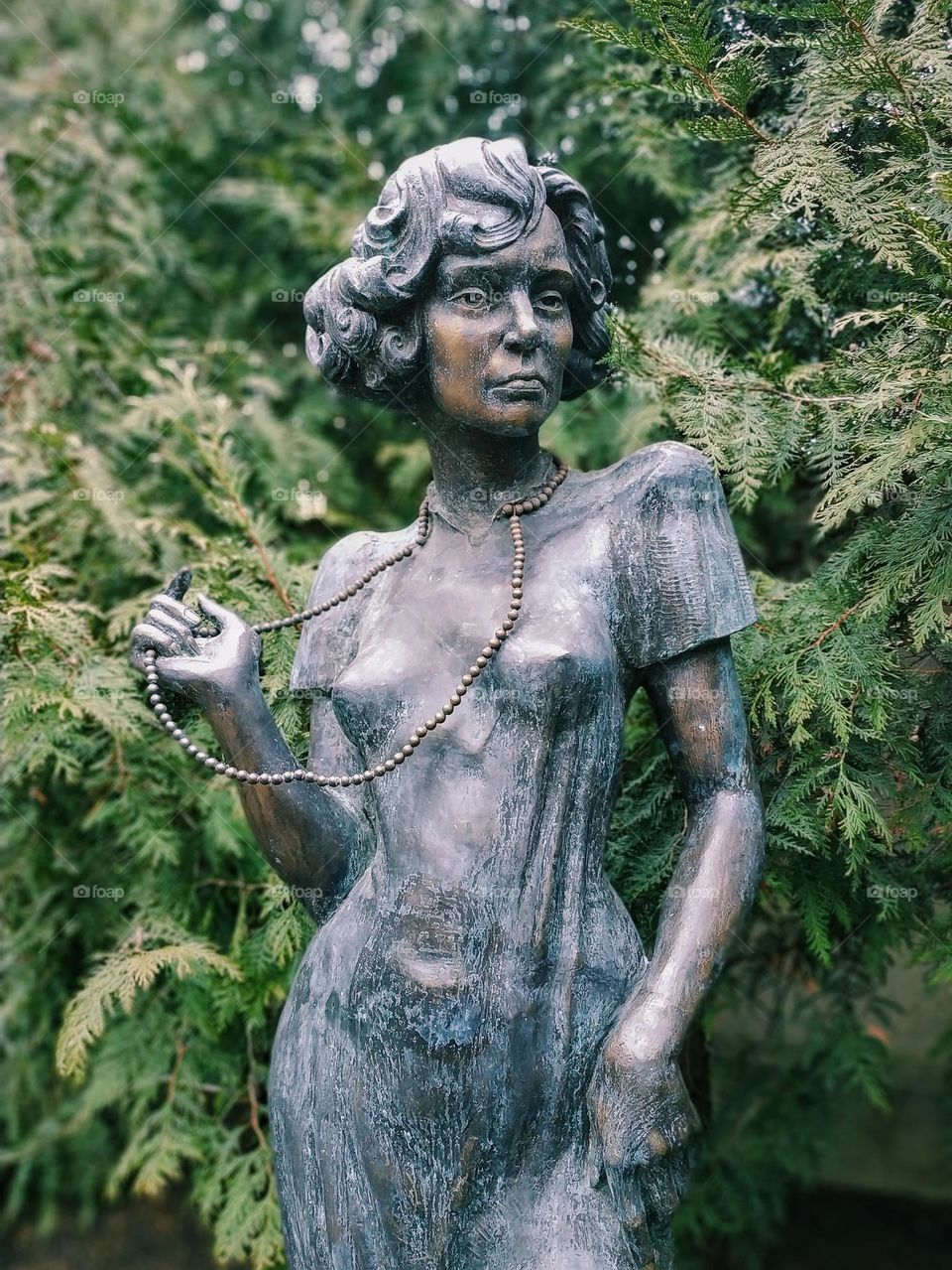 A statue of a woman stands between green fir trees.