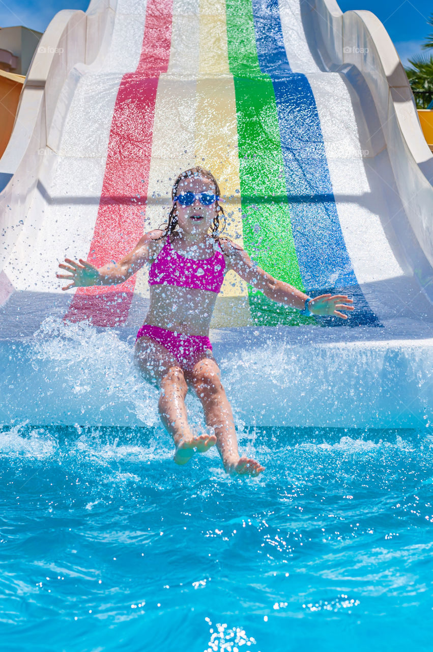 Little girl on rainbow coloured water slide.