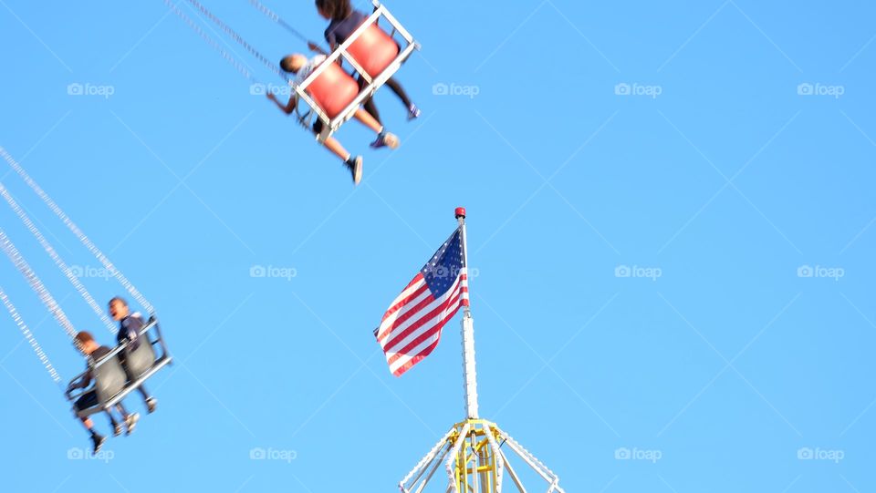 American flag in a July summer fair, children enjoying riding a carousel in the background.