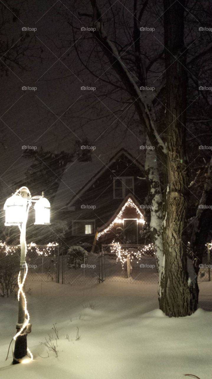 Bright white Christmas lights on a house,  in a snowstorm, street light in front