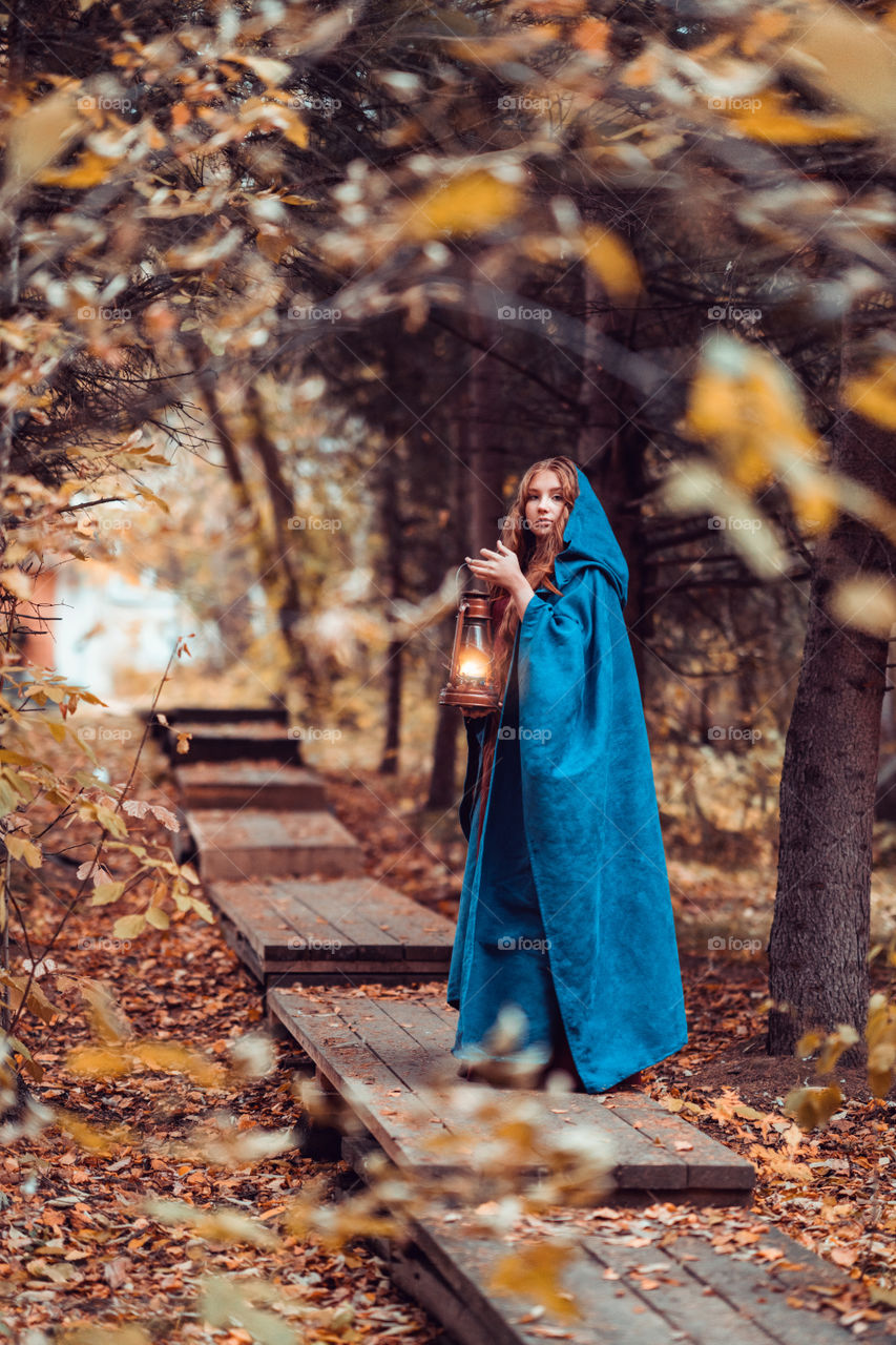 A girl with long red hair and kerosene lamp in a forest