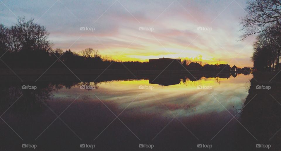 Dramatic and colorful sunset over the river with the gold, yellow, orange, red, purple and blue colors of the sky and the Clouds reflected in the water