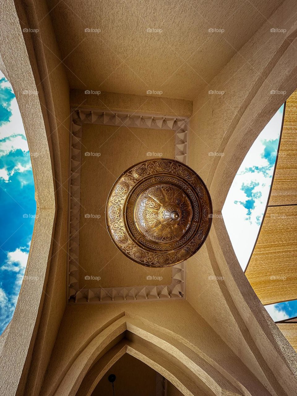 Low shot of a brass lantern in between arches at a mosque, with a hint of sky on both sides 