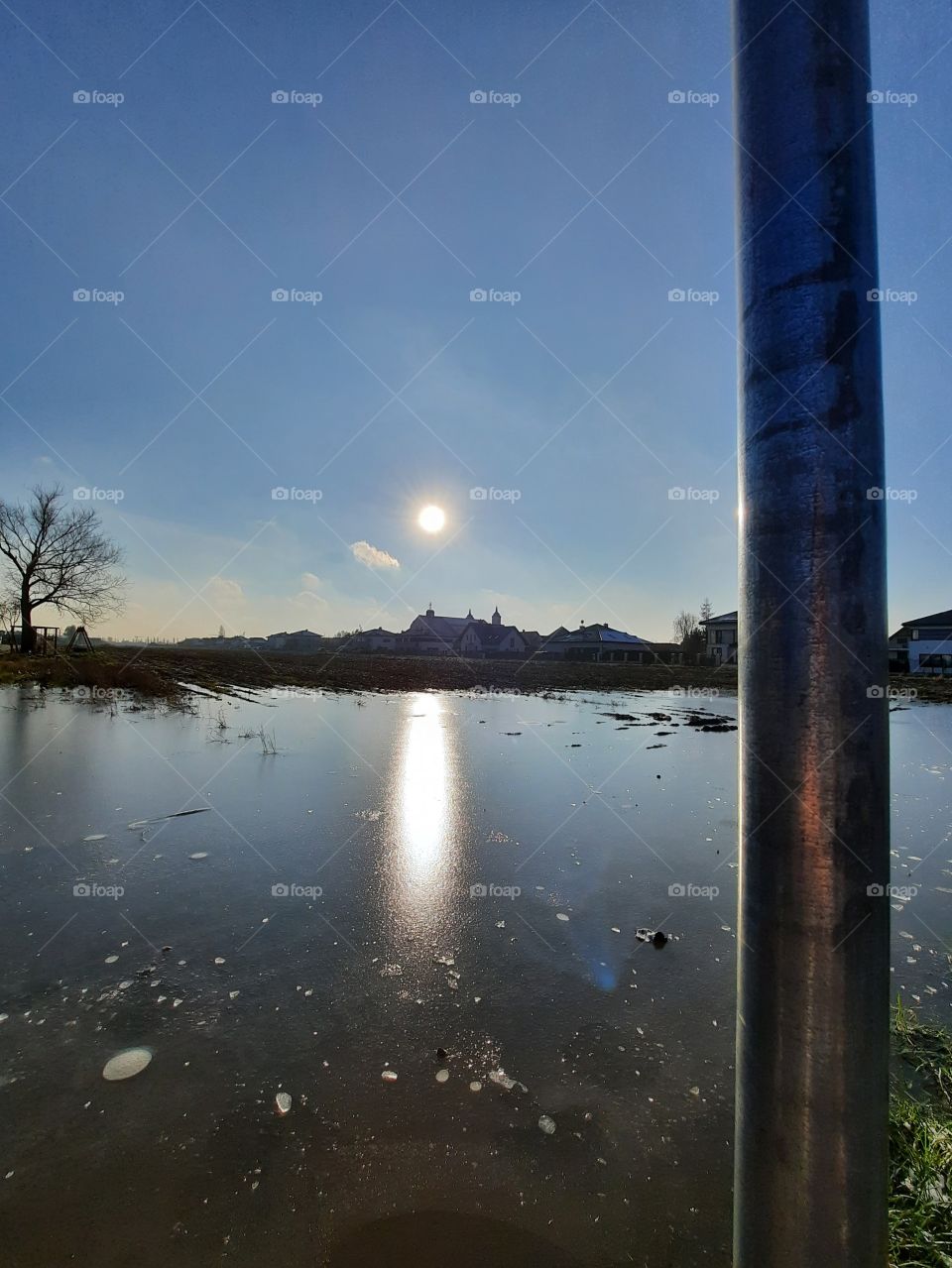 winter day with sun reflection on frozen floaded field and  on metal road sign bar