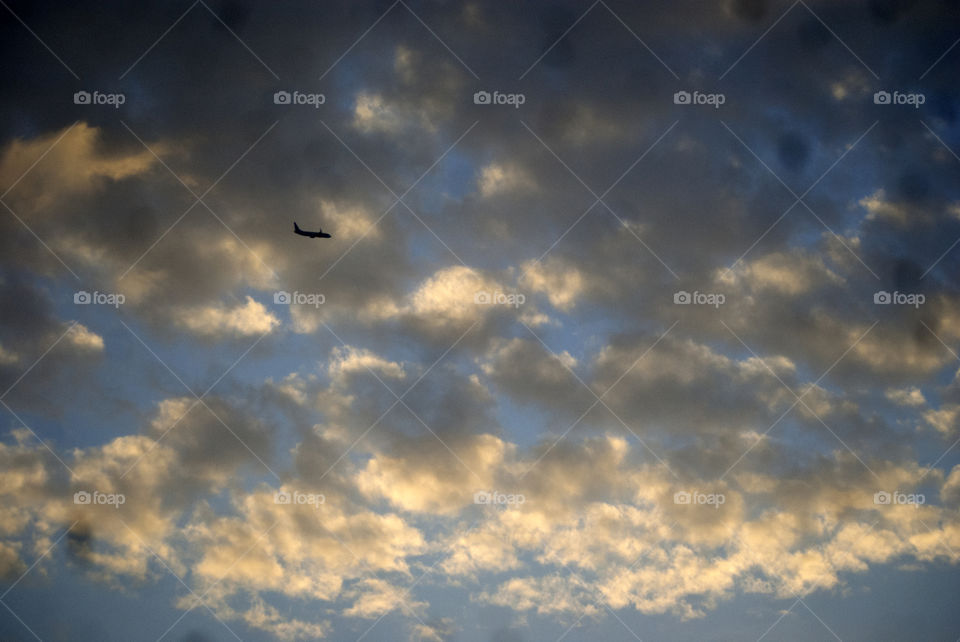 Silhouette of an aeroplane flying to its unknown destination among the evening clouds.