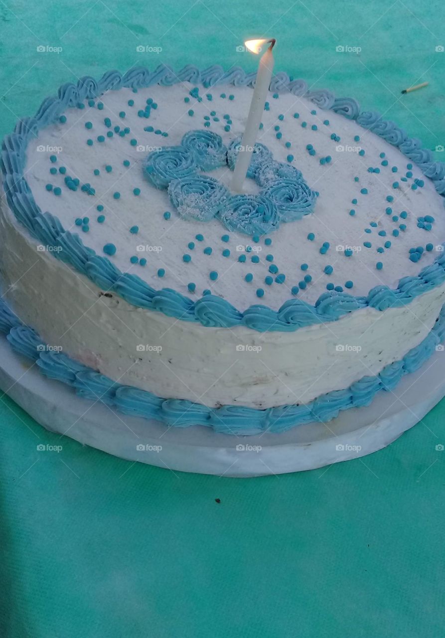 pastel de cumpleaños infantil cubierto por de crema blanca y coloreada de celeste, con una vela en el centro