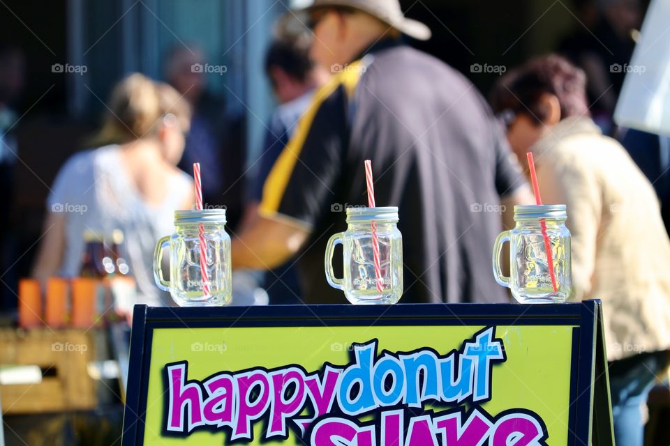 Three glass mason jar drink mugs with straws lined up on sandwich board at concession stand at outdoor festival fair