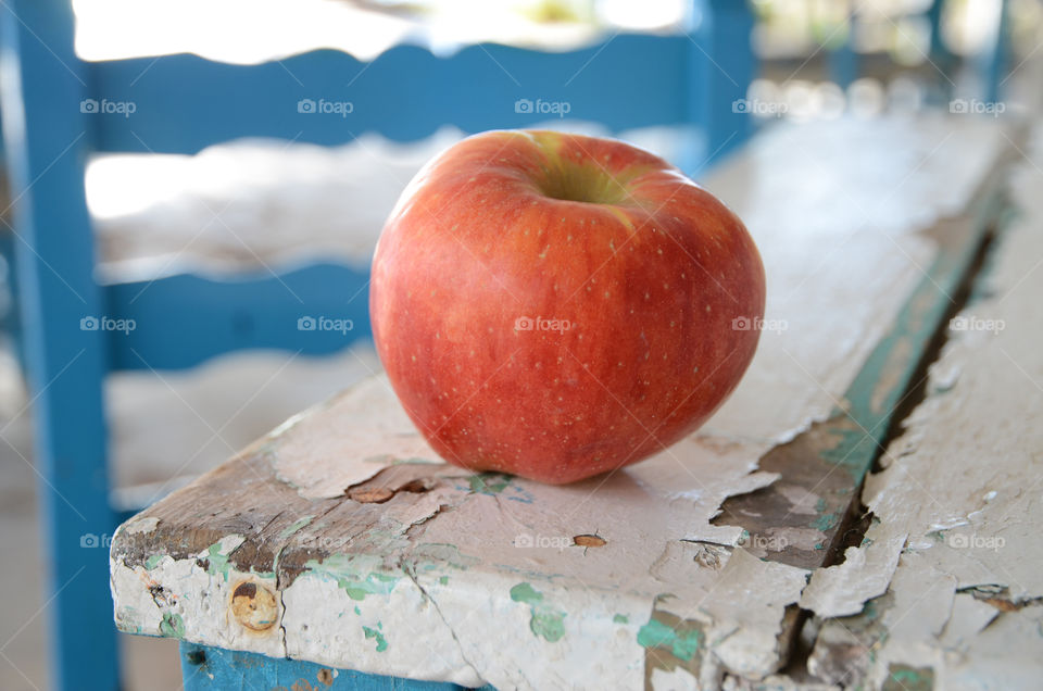 A red apple on a wooden table with a blue chair in the background 