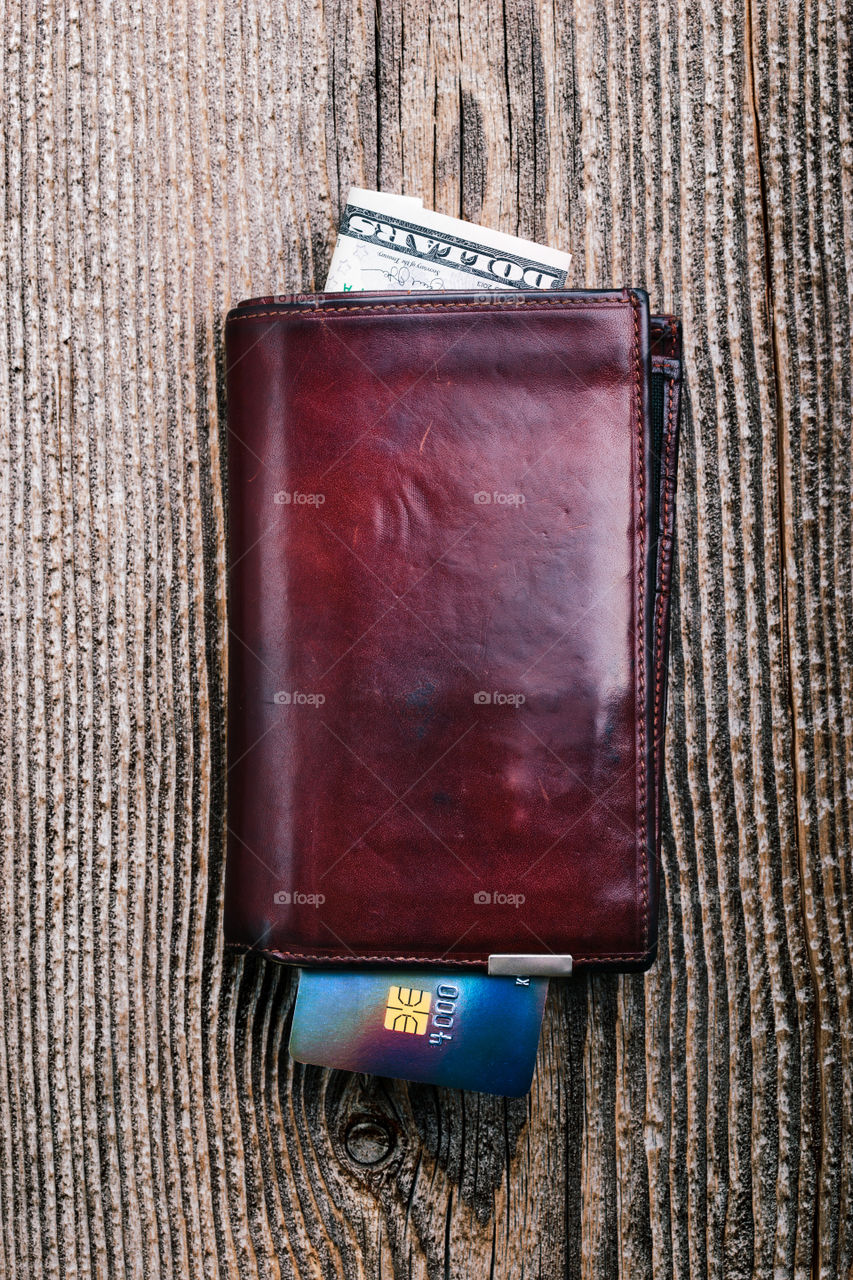 Leather wallet with dollar banknotes, credit card on wooden desk. Portrait orientation