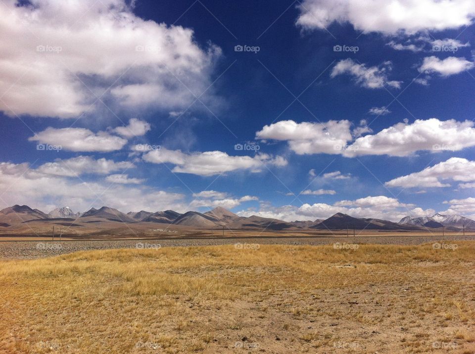 Tibetan landscape with cloudy sky and mountain peaks and fields