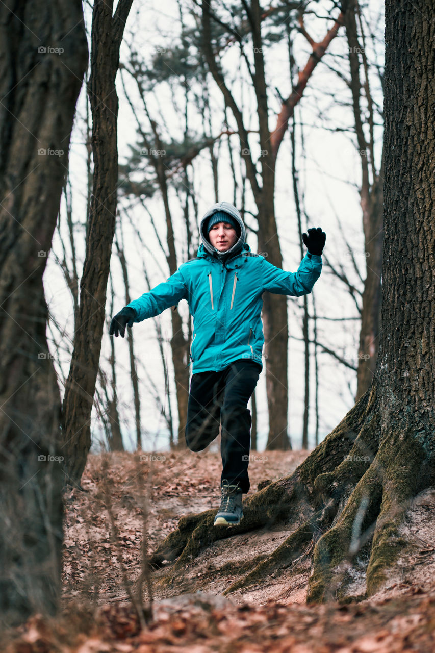 Young man running outdoors during workout in a forest among leafless trees on cold freeze autumn day. Boy is wearing sport clothes