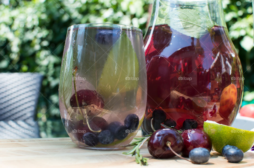 Refreshing summertime detox drinks on table garnished with lime, mint, blueberry and dark red cherry outdoors for summer party gourmet drink epicure photography