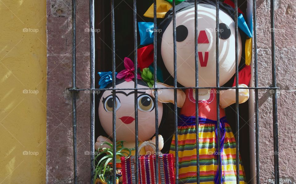 Two colorful  Mexican dolls looking out the window onto the street in San Miguel de Allende, Mexico.