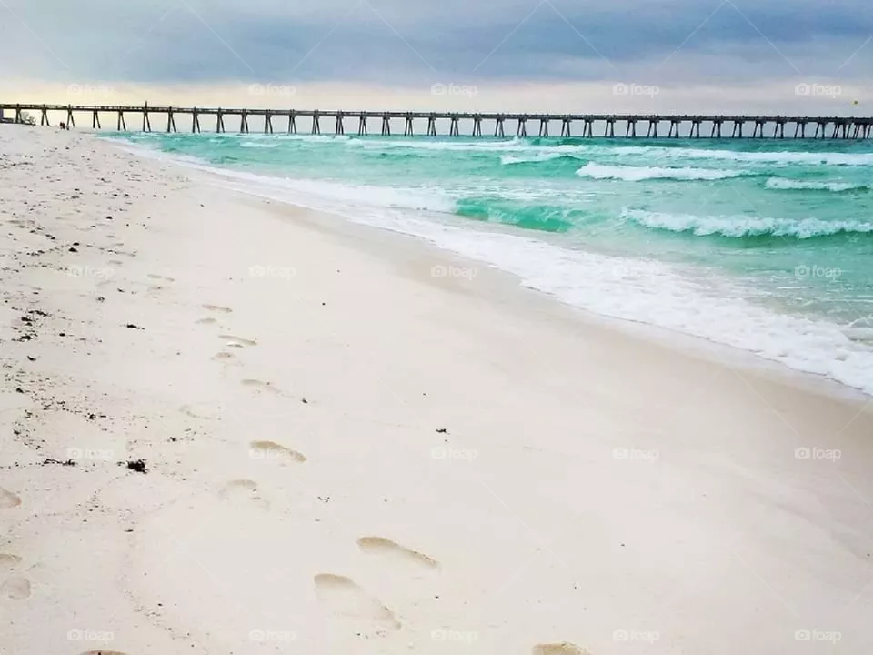 footprints in white sand by pier